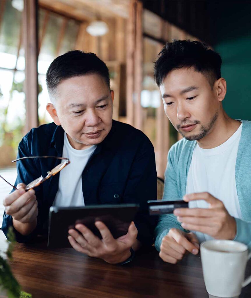 Two financial professionals reviewing information on a tablet and credit card during a client advisory meeting in a café setting — representing personalised wealth management and financial planning conversations